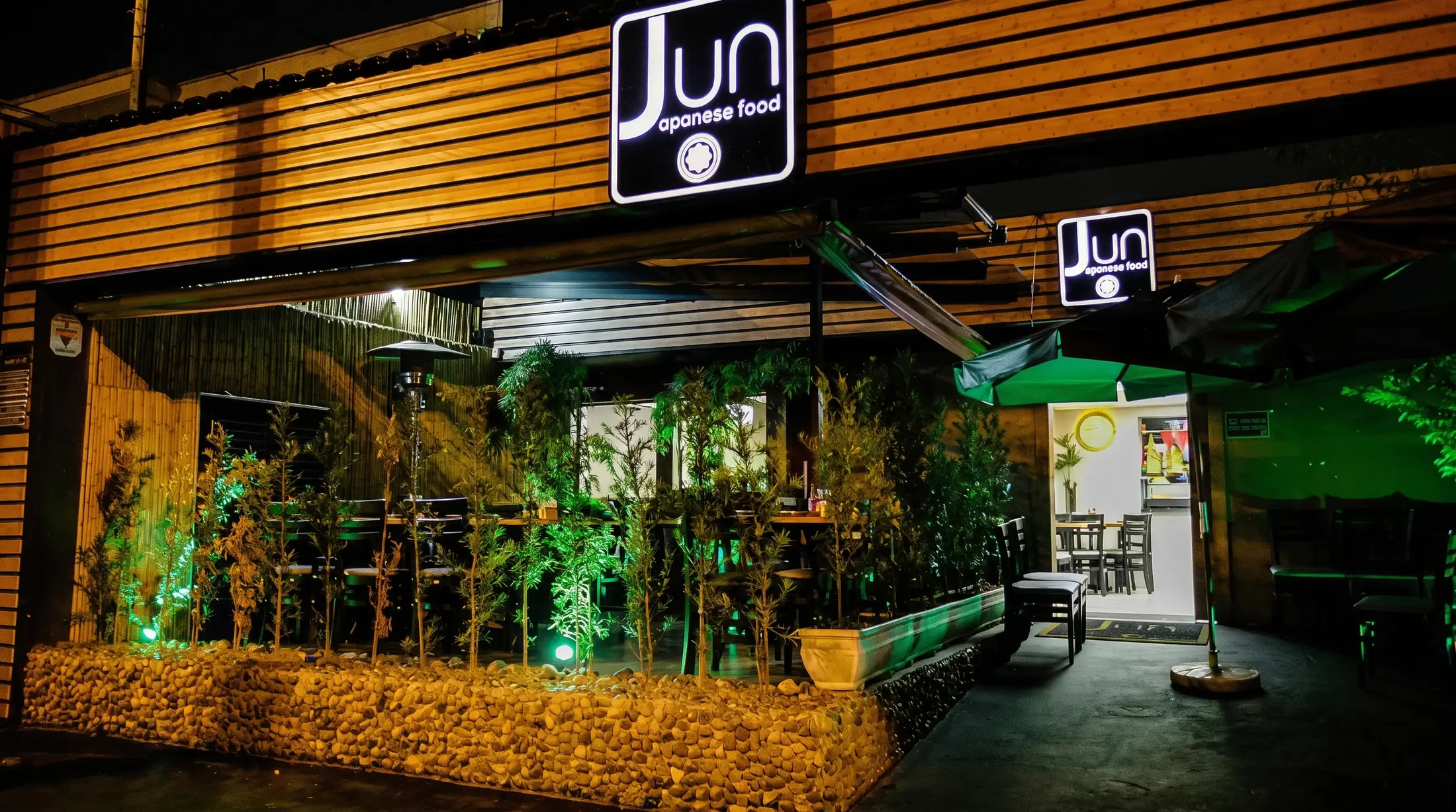 Fachada de restaurante com comunicação visual iluminada, marcenaria em ripado de madeira e paisagismo, projeto comercial assinado pela LaArc
