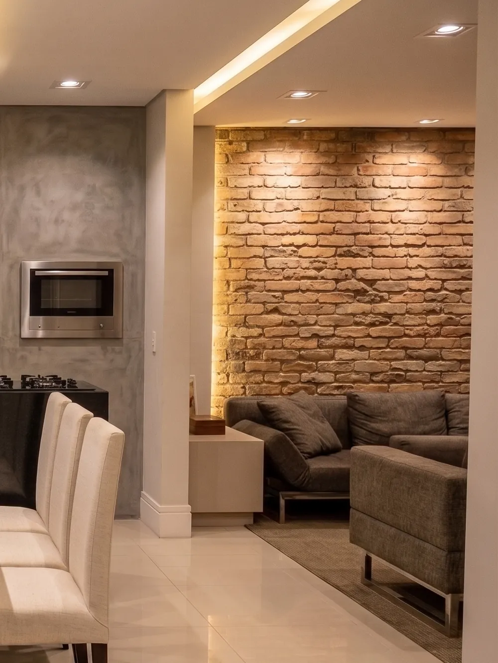 Sala de estar com parede de tijolo aparente iluminada e sofá em projeto residencial da LaArc