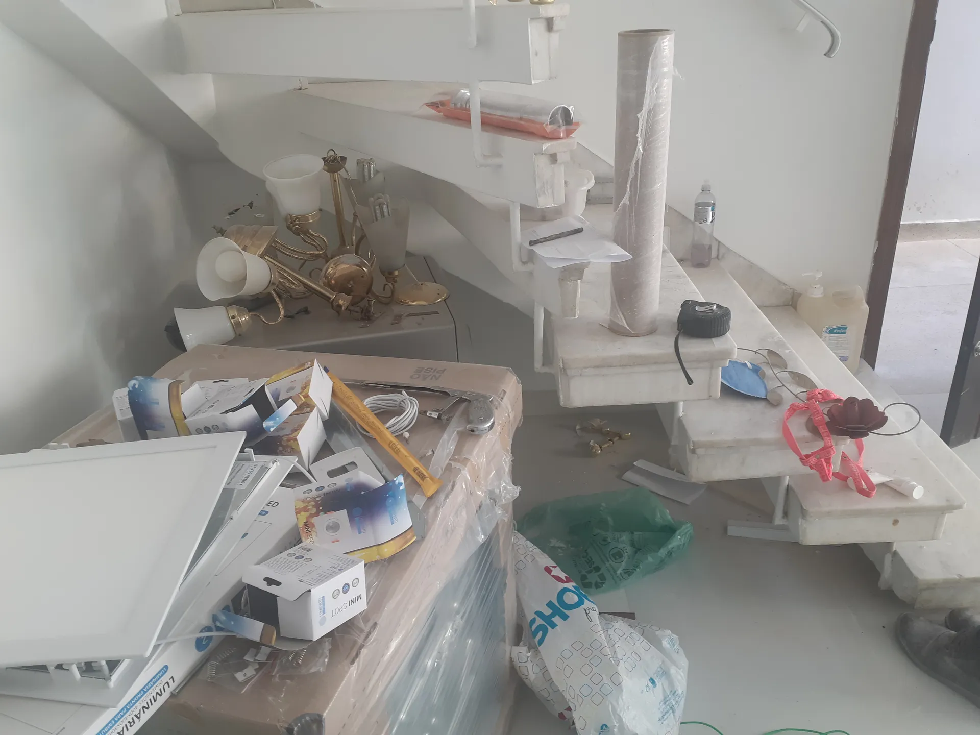 Espaço embaixo da escada do sobrado durante a obra, ocupado por caixas, luminárias e materiais