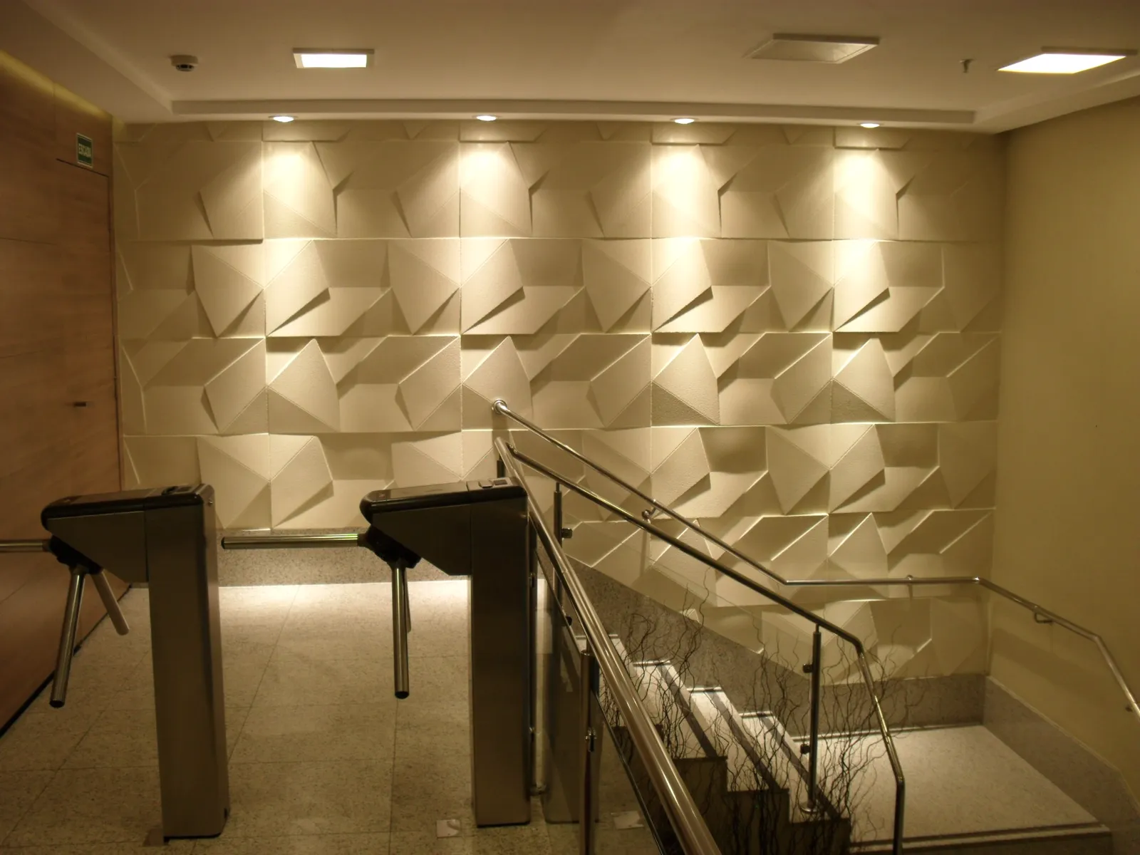 Hall de entrada de condomínio com parede de revestimento 3D iluminada, catracas e escada com guarda-corpo de vidro, obra executada pela LaArc
