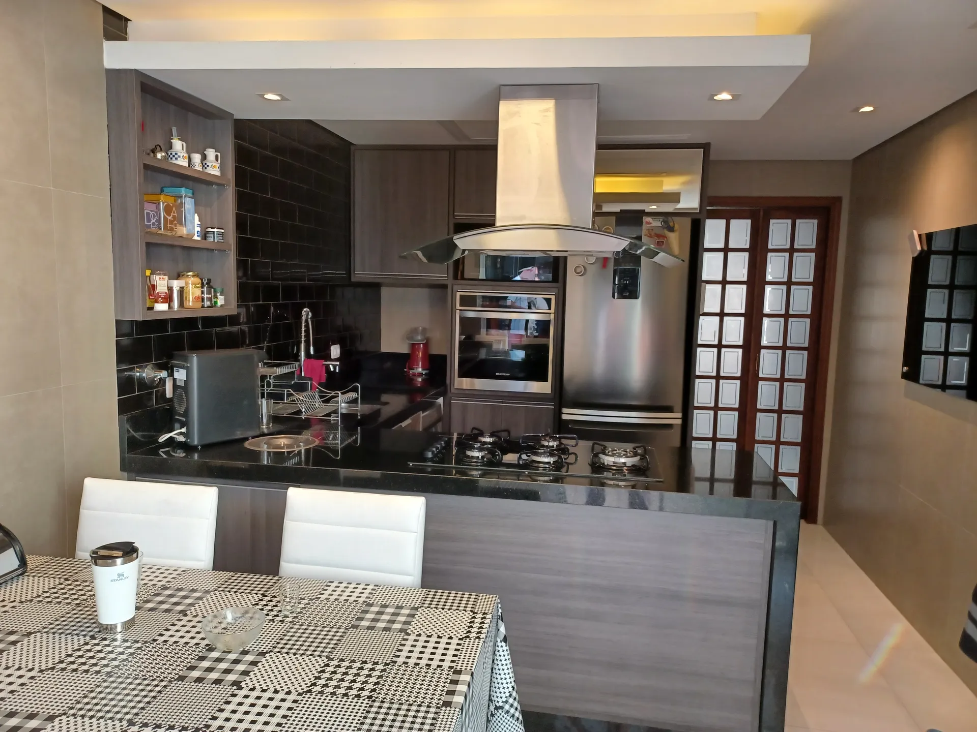 Cozinha da casa pronta, com tijolinho preto, ilha com cooktop e coifa inox, executada conforme o projeto da LaArc