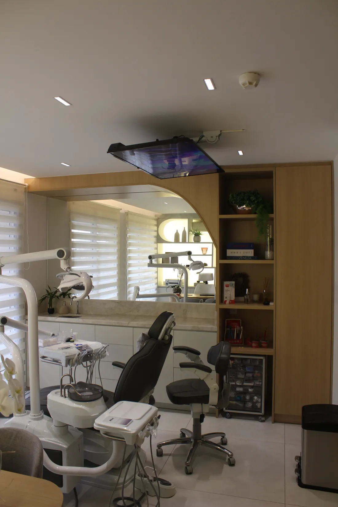 Sala clínica odontológica com painel em arco de madeira, nichos e armários planejados ao lado da cadeira